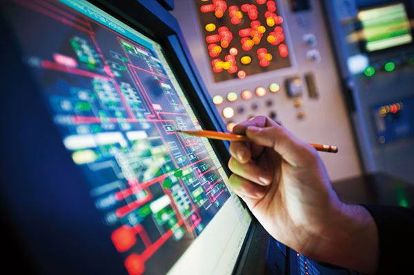hand holding pencil pointing to oil refinery control room screen